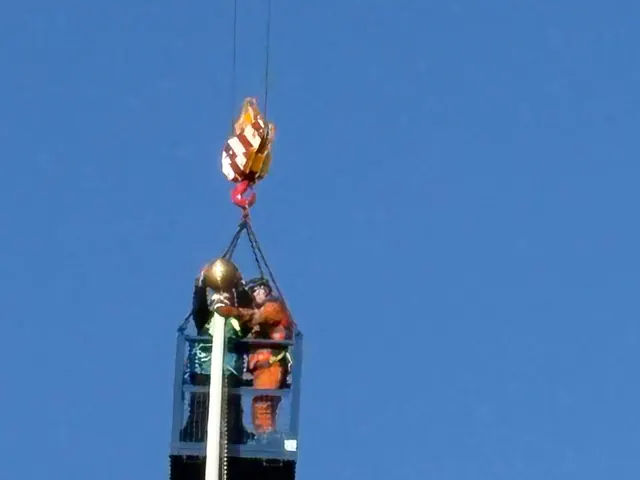 Two of the crew in a crane basket setting the finial on a tall commercial pole.