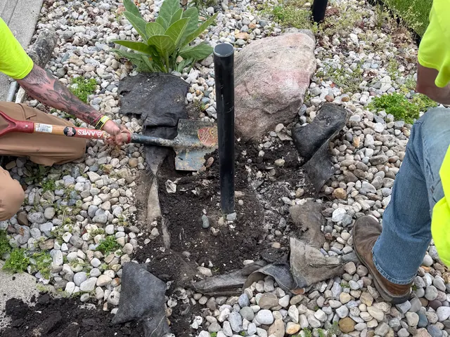Setting a ground sleeve by hand in a landscaped bed.