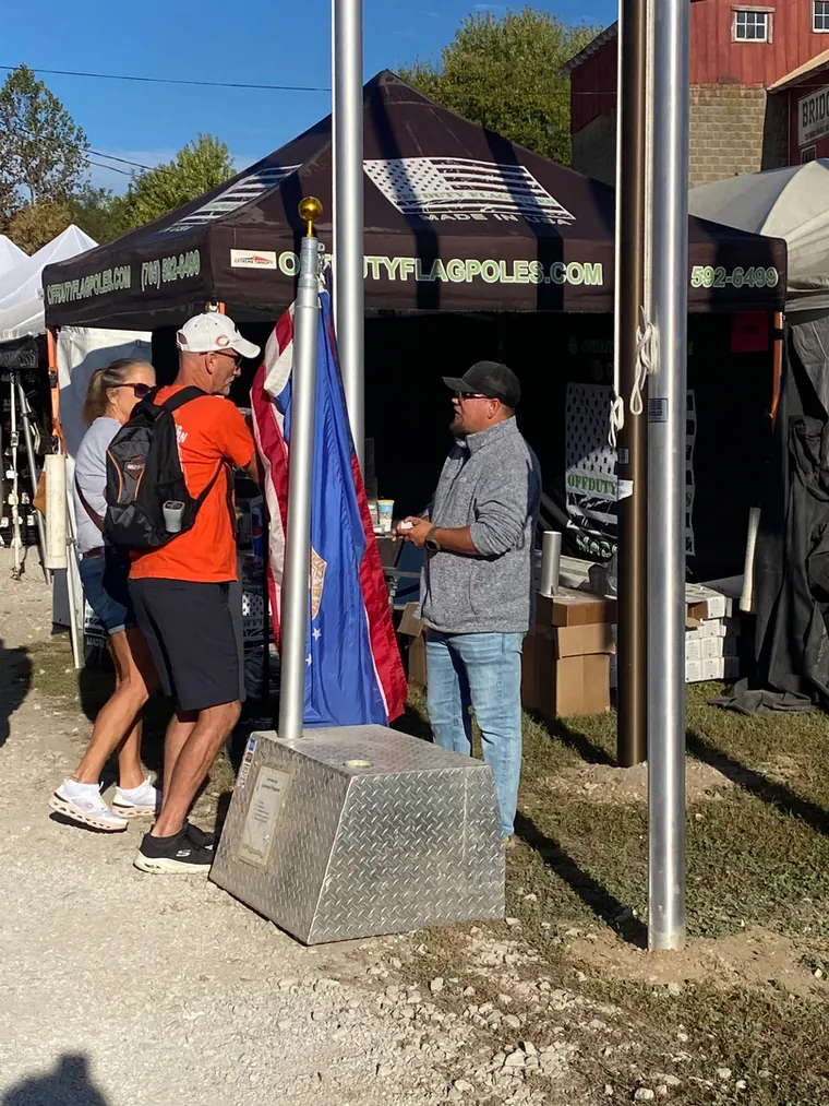 The Off Duty Flagpoles stand at an Indiana festival with flags and poles on display